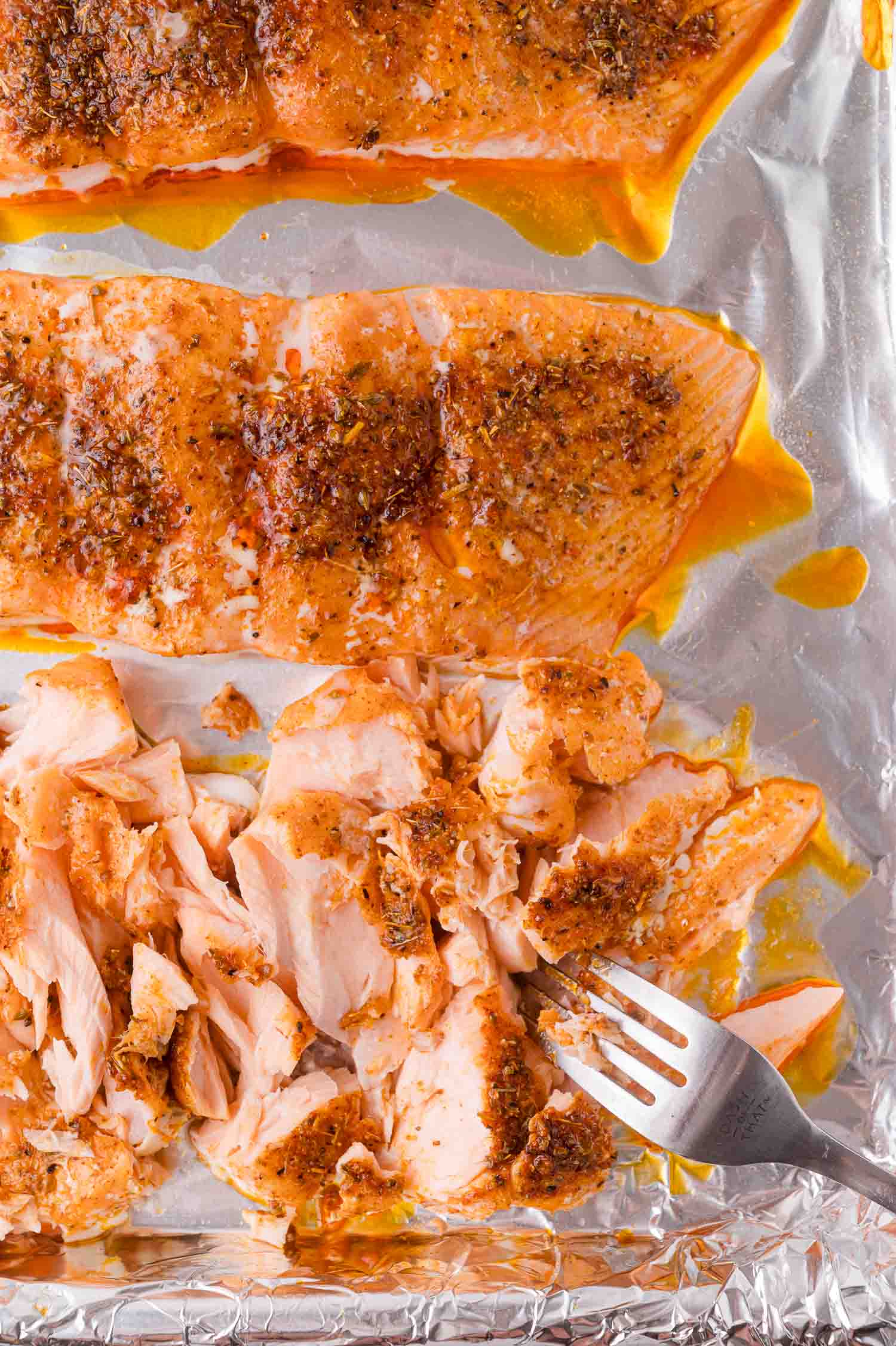 Two baked salmon fillets on foil, one fillet partially flaked with a fork.