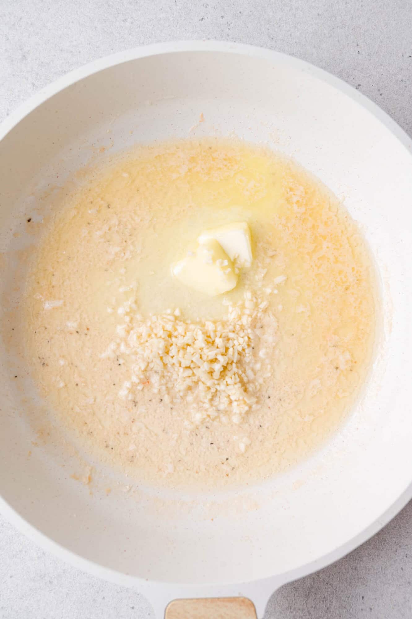 A white pan with melted butter and minced garlic cooking on the surface.