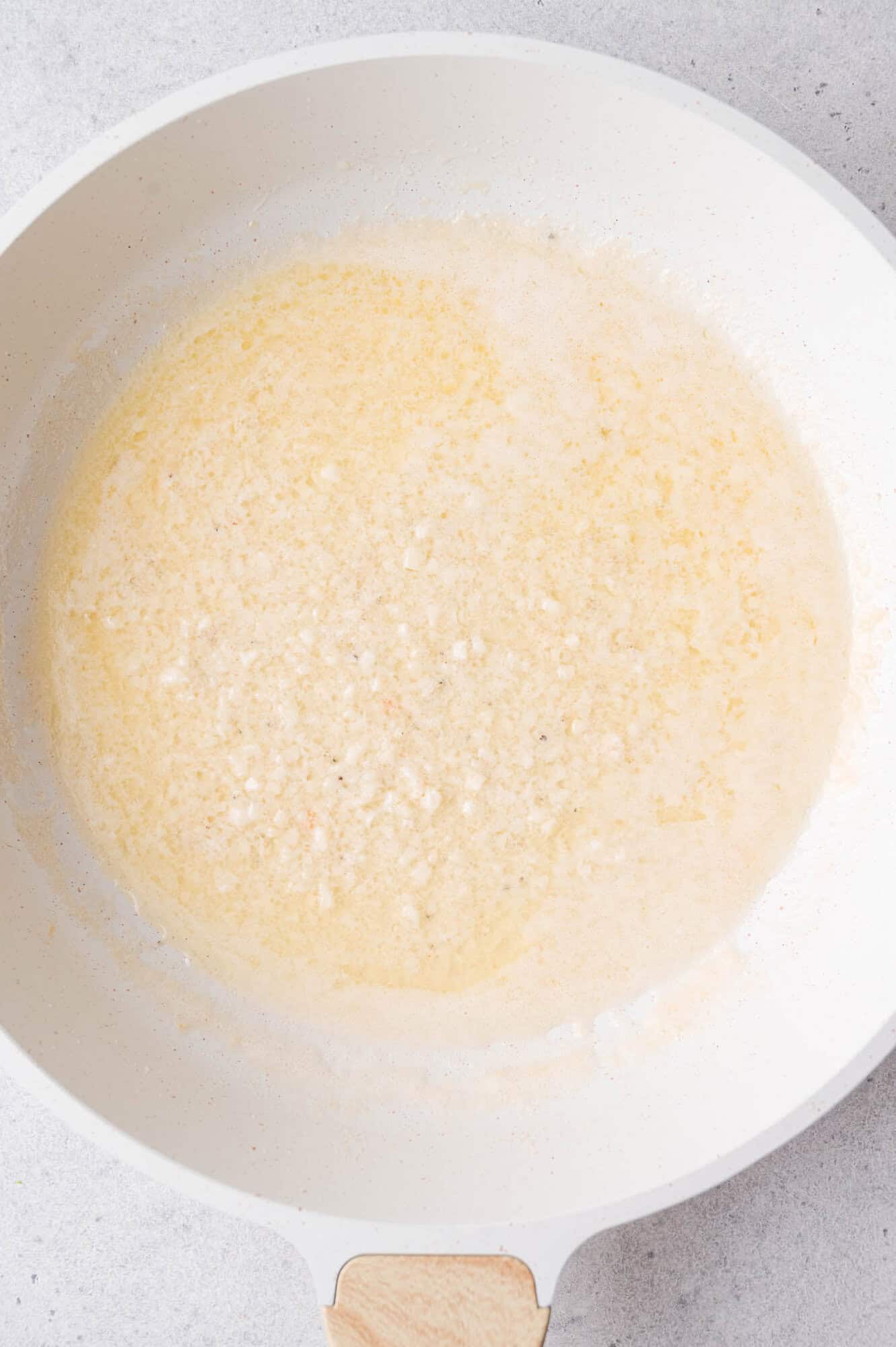 A white skillet with melted butter and garlic, being sautéed over medium heat.
