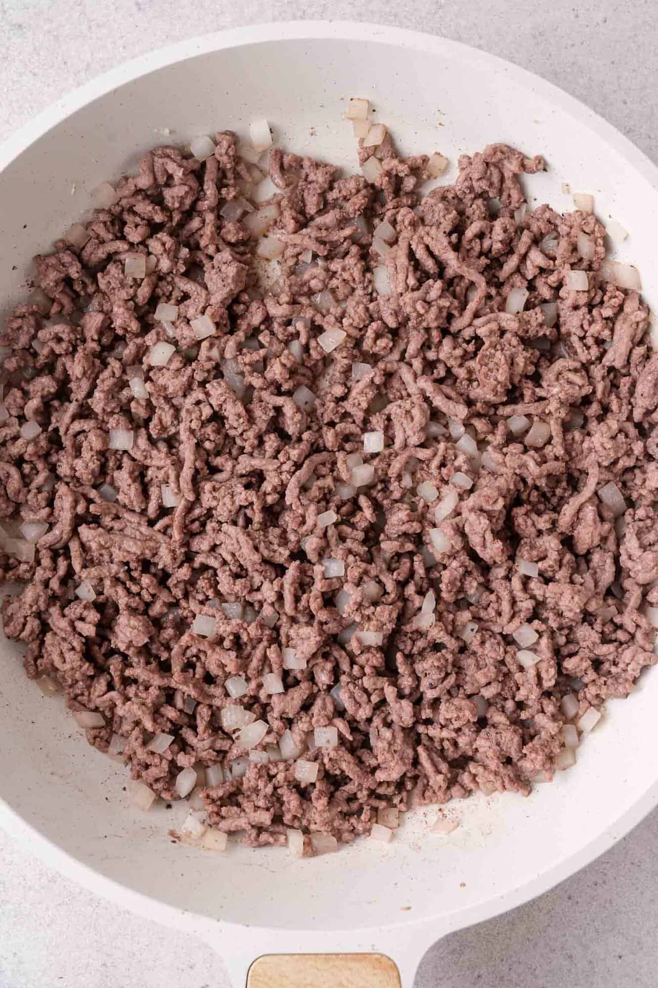 Cooked ground beef and chopped onions in a white skillet, viewed from above.
