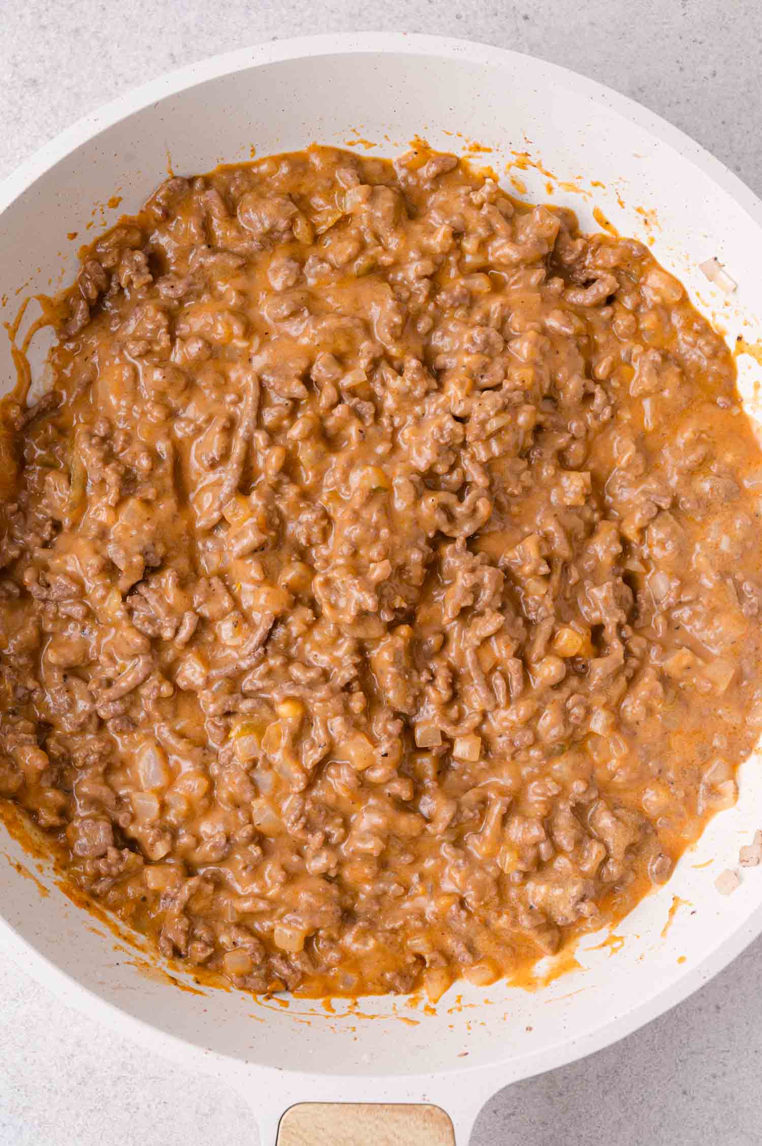 Ground beef in a creamy sauce cooking in a white skillet, with visible pieces of beef and a thick, orange-brown gravy.