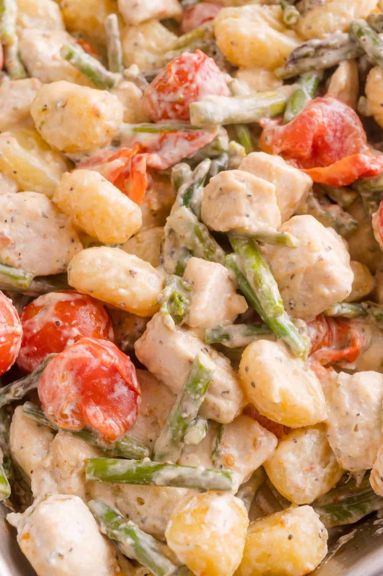 Creamy gnocchi dish with chunks of chicken, halved cherry tomatoes, asparagus pieces, and a white sauce, all mixed together.