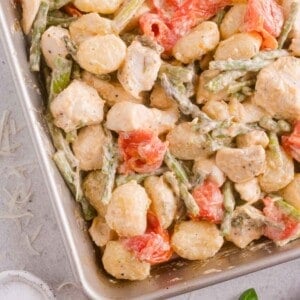 Baked gnocchi with pieces of chicken, asparagus, and cherry tomatoes in a creamy sauce, shown in a baking dish.