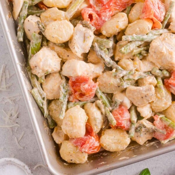 Baked gnocchi with pieces of chicken, asparagus, and cherry tomatoes in a creamy sauce, shown in a baking dish.