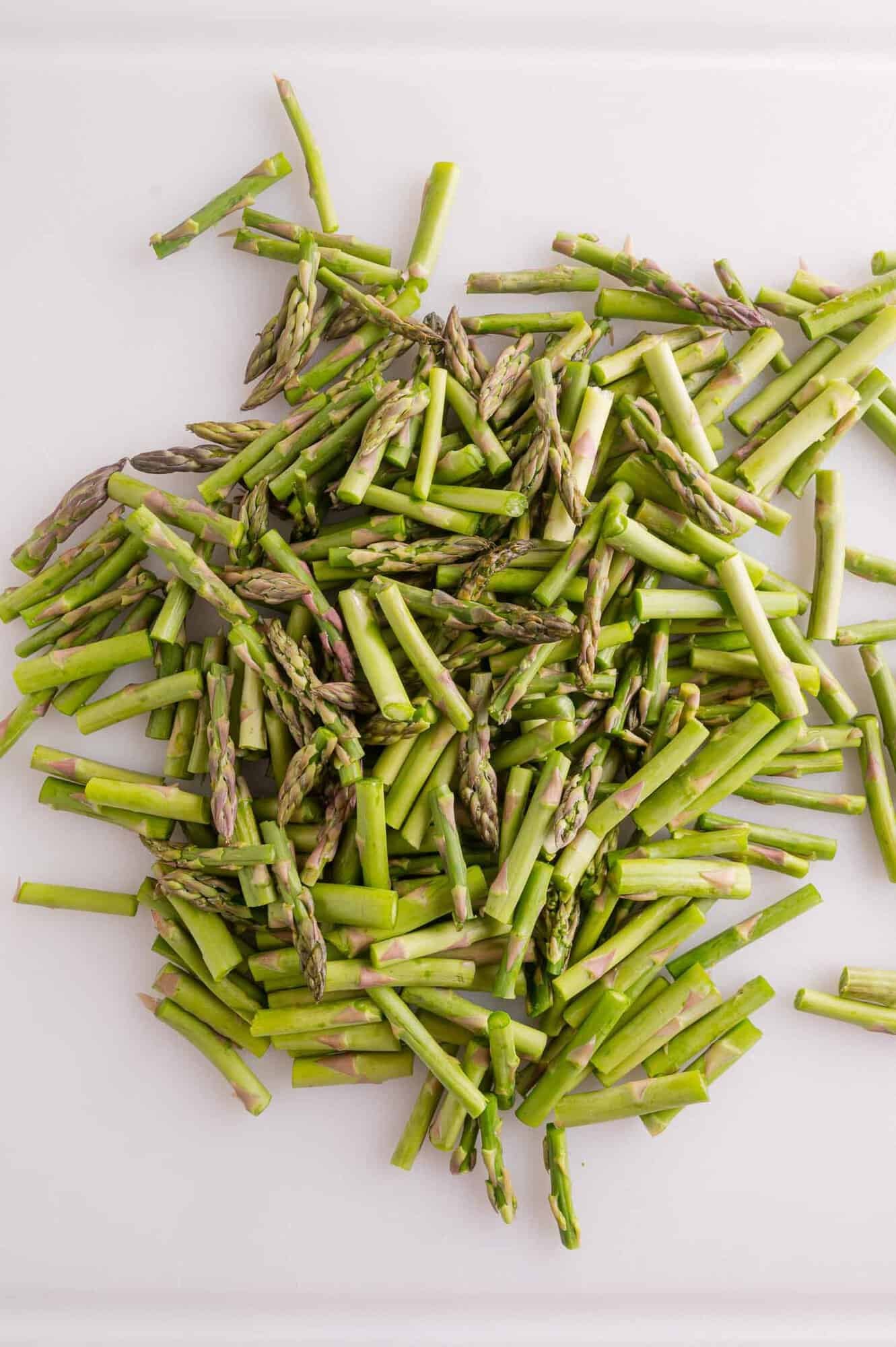 Chopped asparagus spears scattered on a white surface.