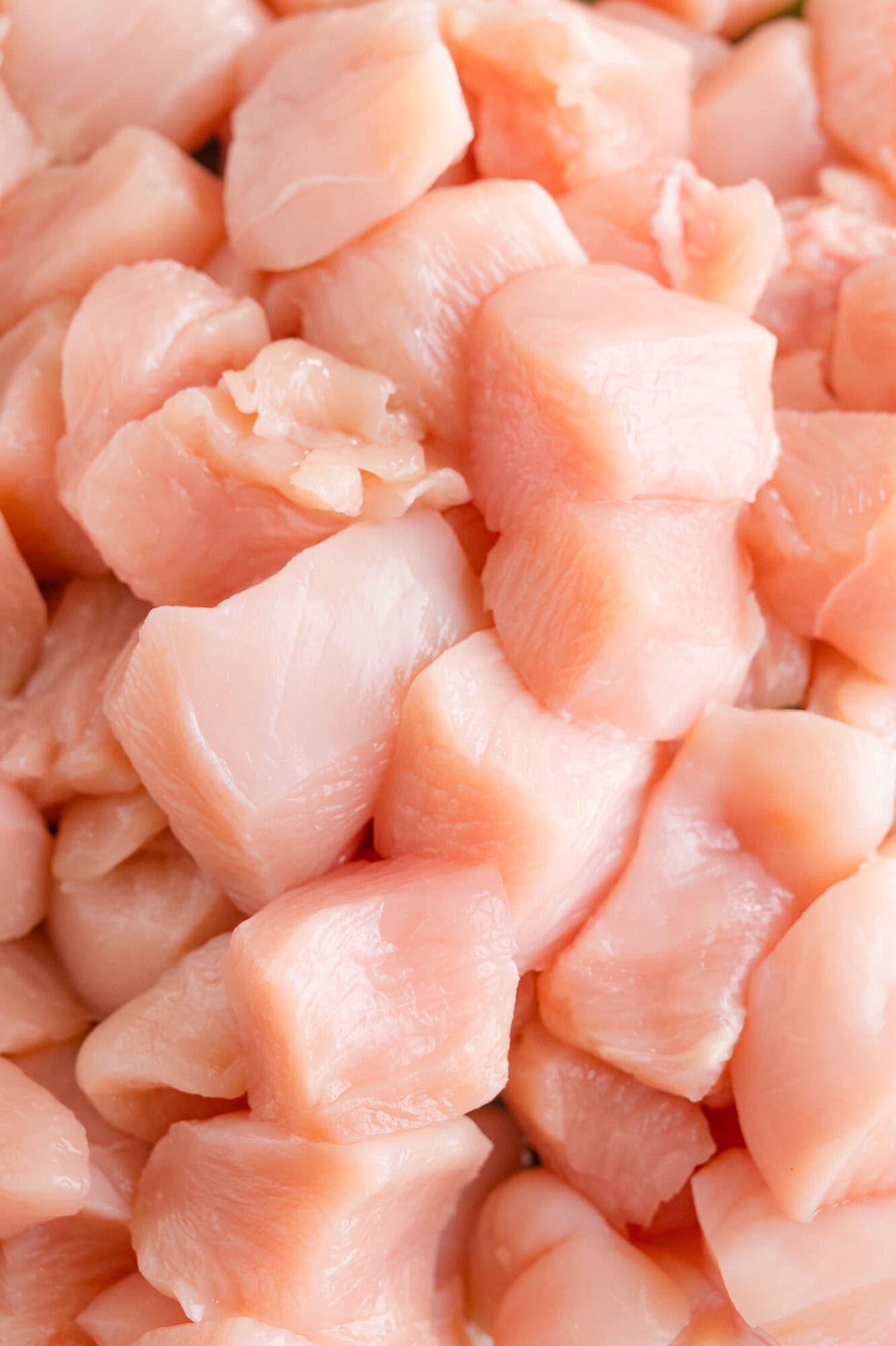 Close-up of raw, boneless, skinless chicken breast pieces cut into cubes, arranged in a pile.