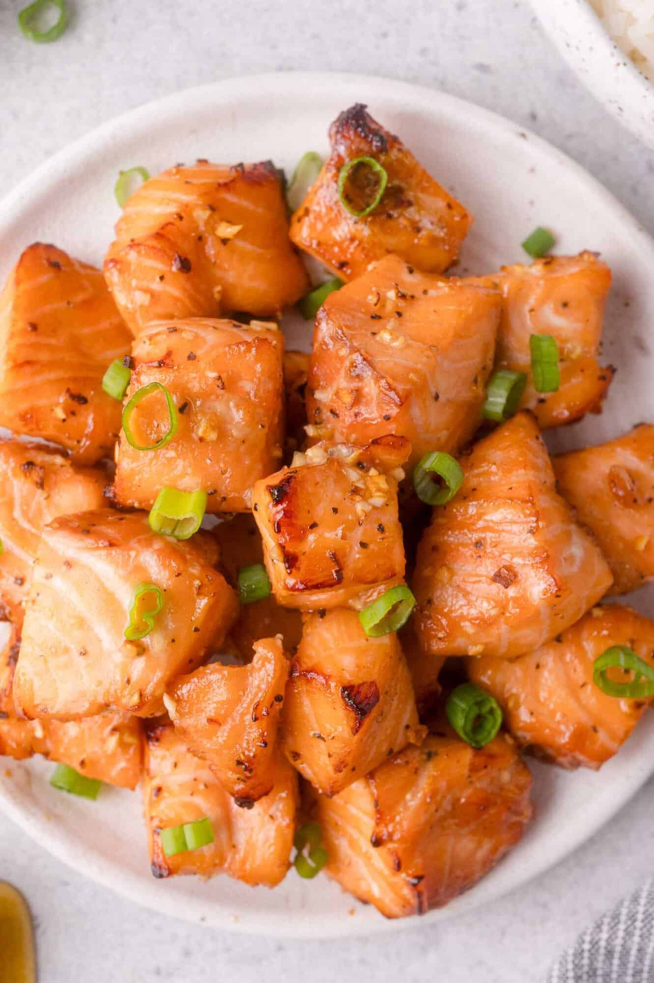 A white plate with air fryer salmon bites, garnished with chopped green onions.