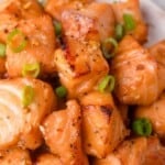 Close-up of cooked salmon cubes seasoned with honey garlic sauce and garnished with chopped green onions.