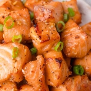 Close-up of cooked salmon cubes seasoned with honey garlic sauce and garnished with chopped green onions.