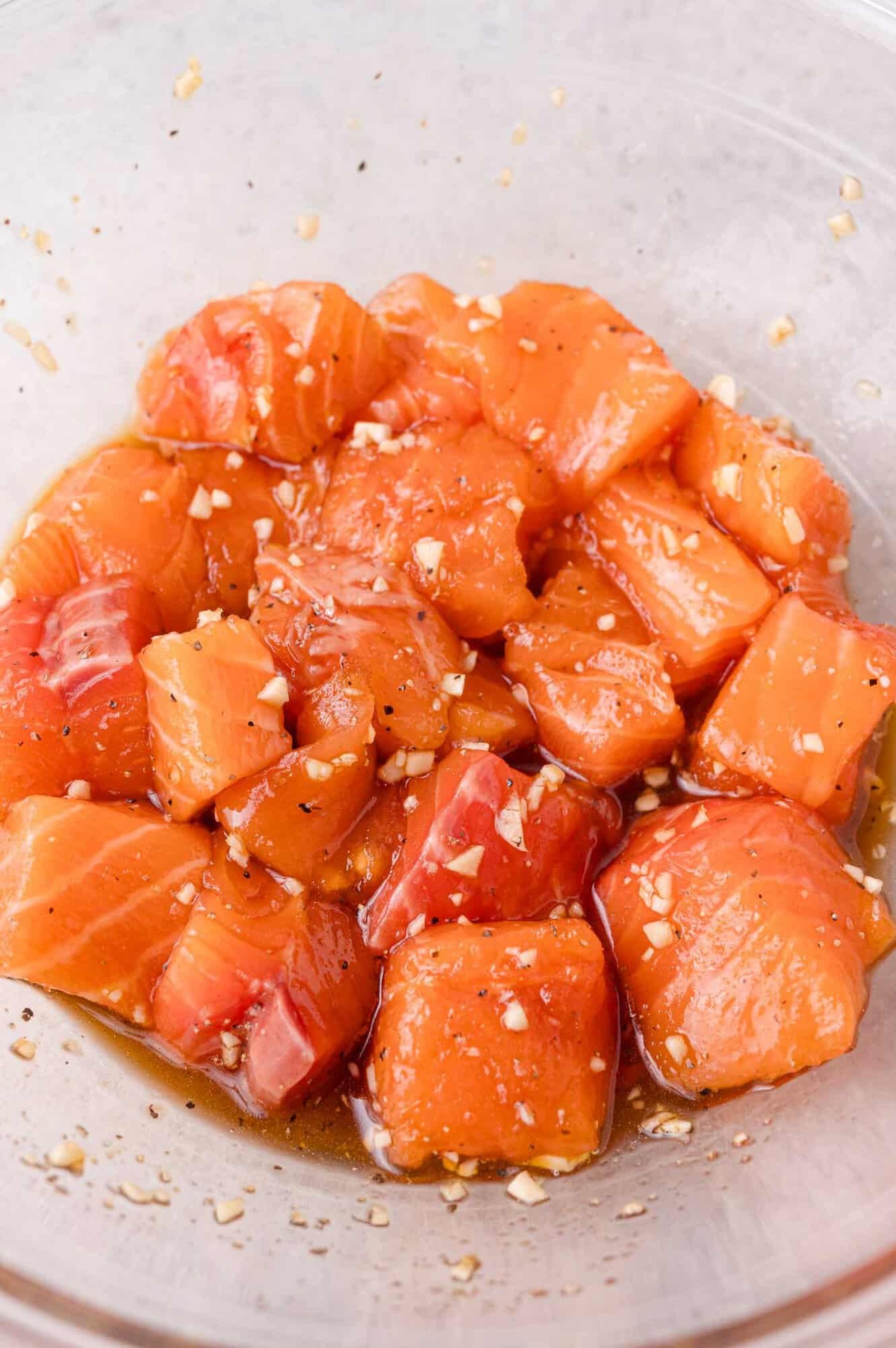 Cubes of raw salmon marinated with sauce and minced garlic in a clear glass bowl.
