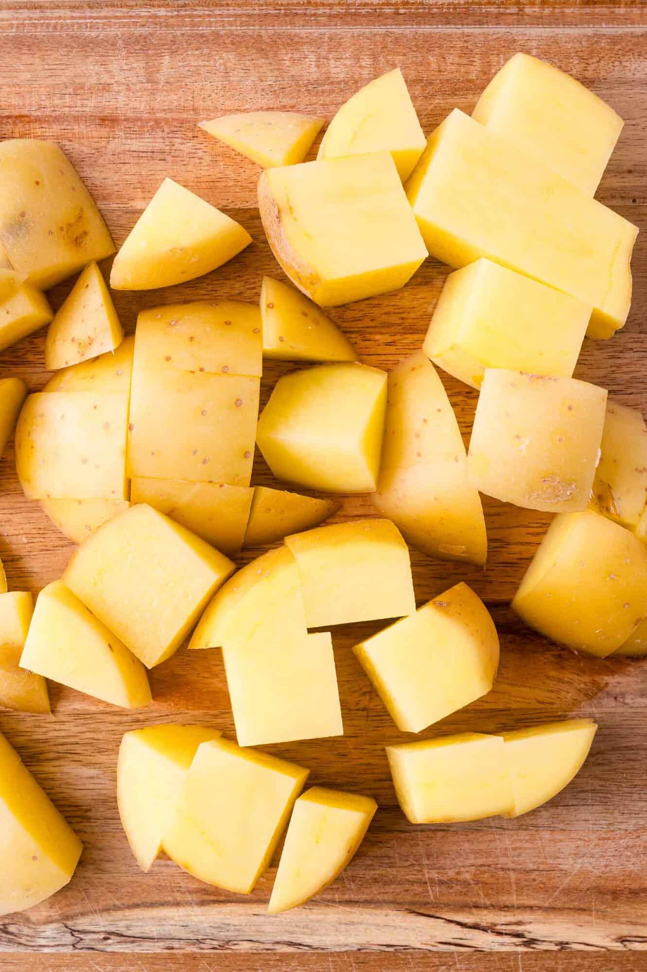 Chopped yellow potatoes with skin on, arranged on a wooden cutting board.