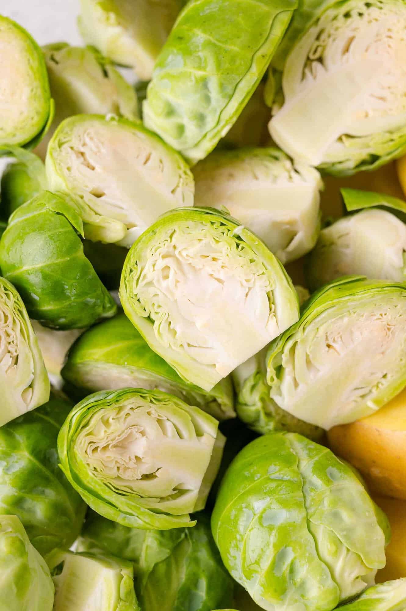 Close-up of fresh Brussels sprouts, some whole and some halved, showing their light green leaves and dense interiors.