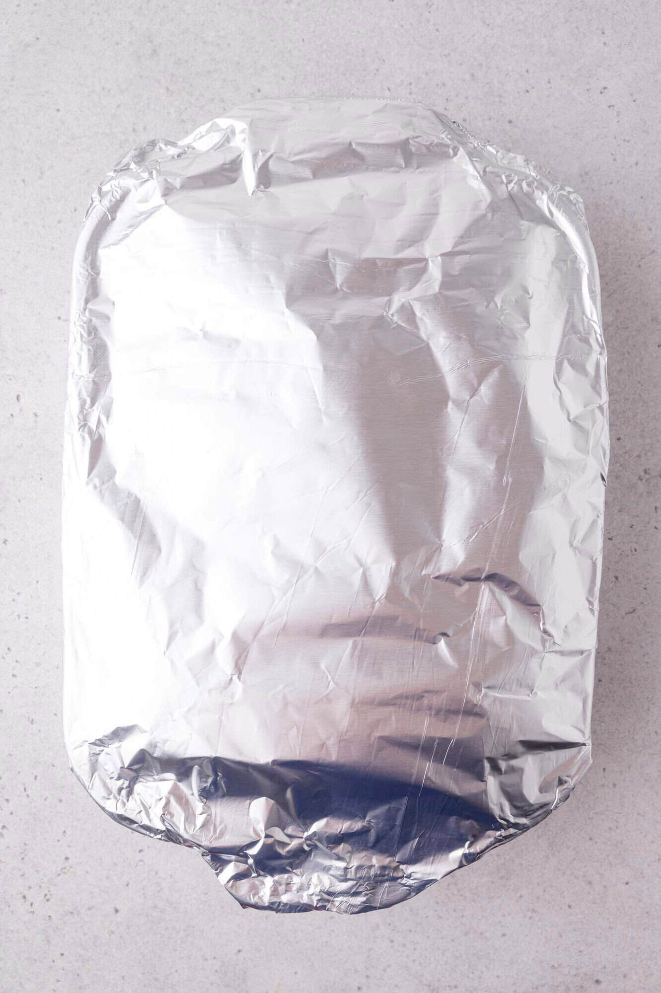 A rectangular baking dish covered tightly with aluminum foil sits on a light-colored countertop.