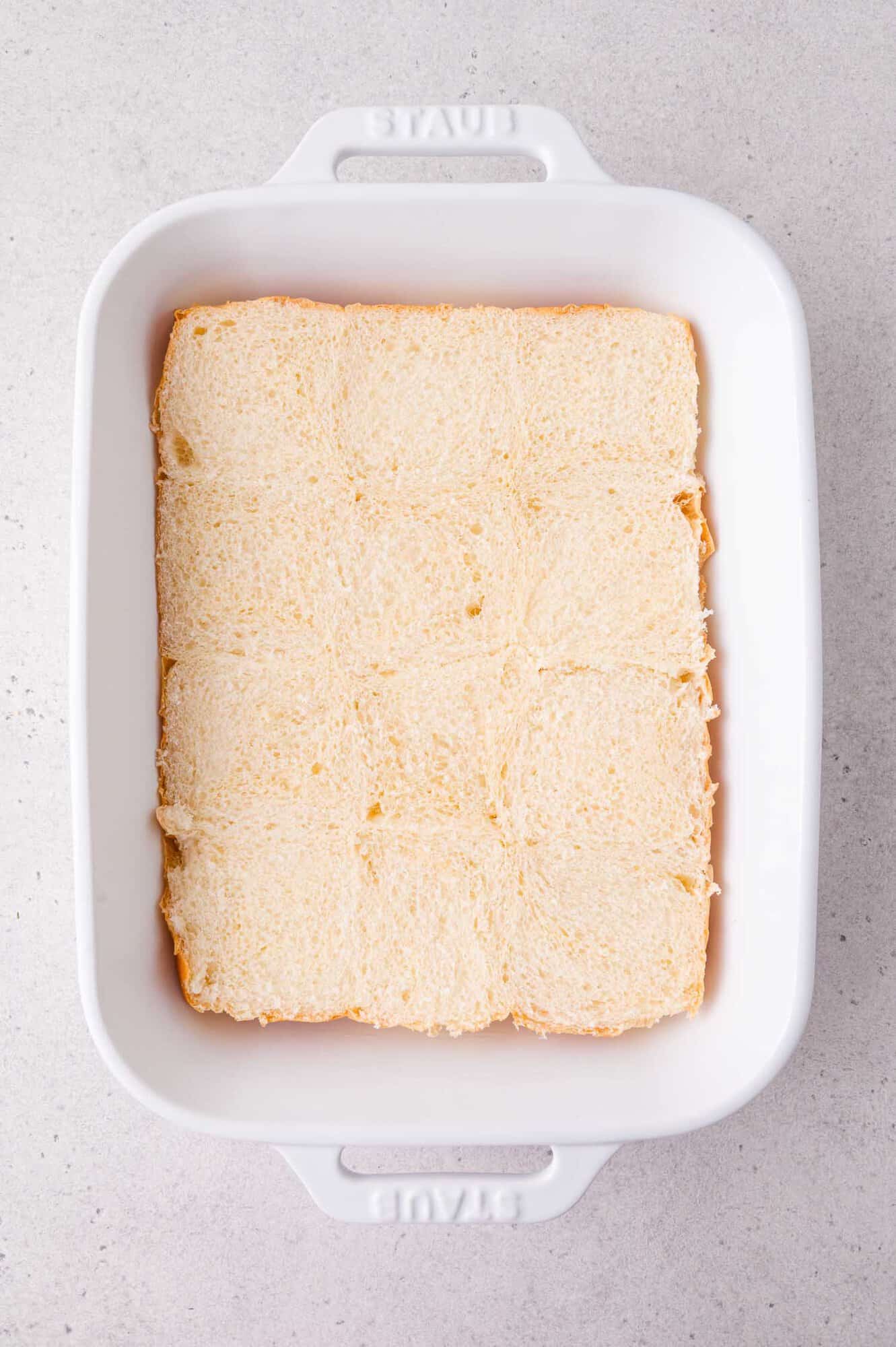 A white baking dish filled with slider rolls on a light gray surface.