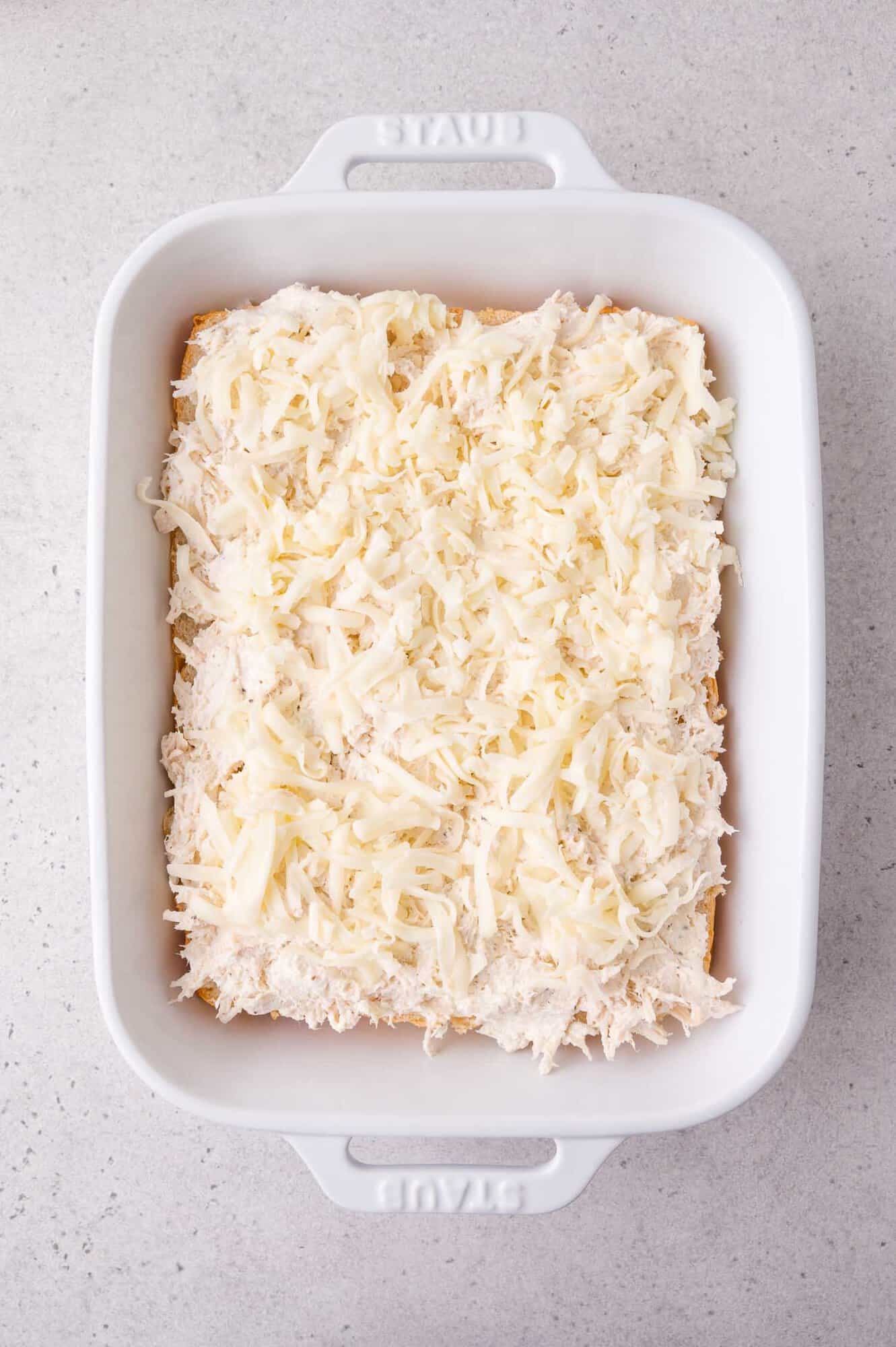 White ceramic baking dish filled with shredded cheese evenly spread over sliders.