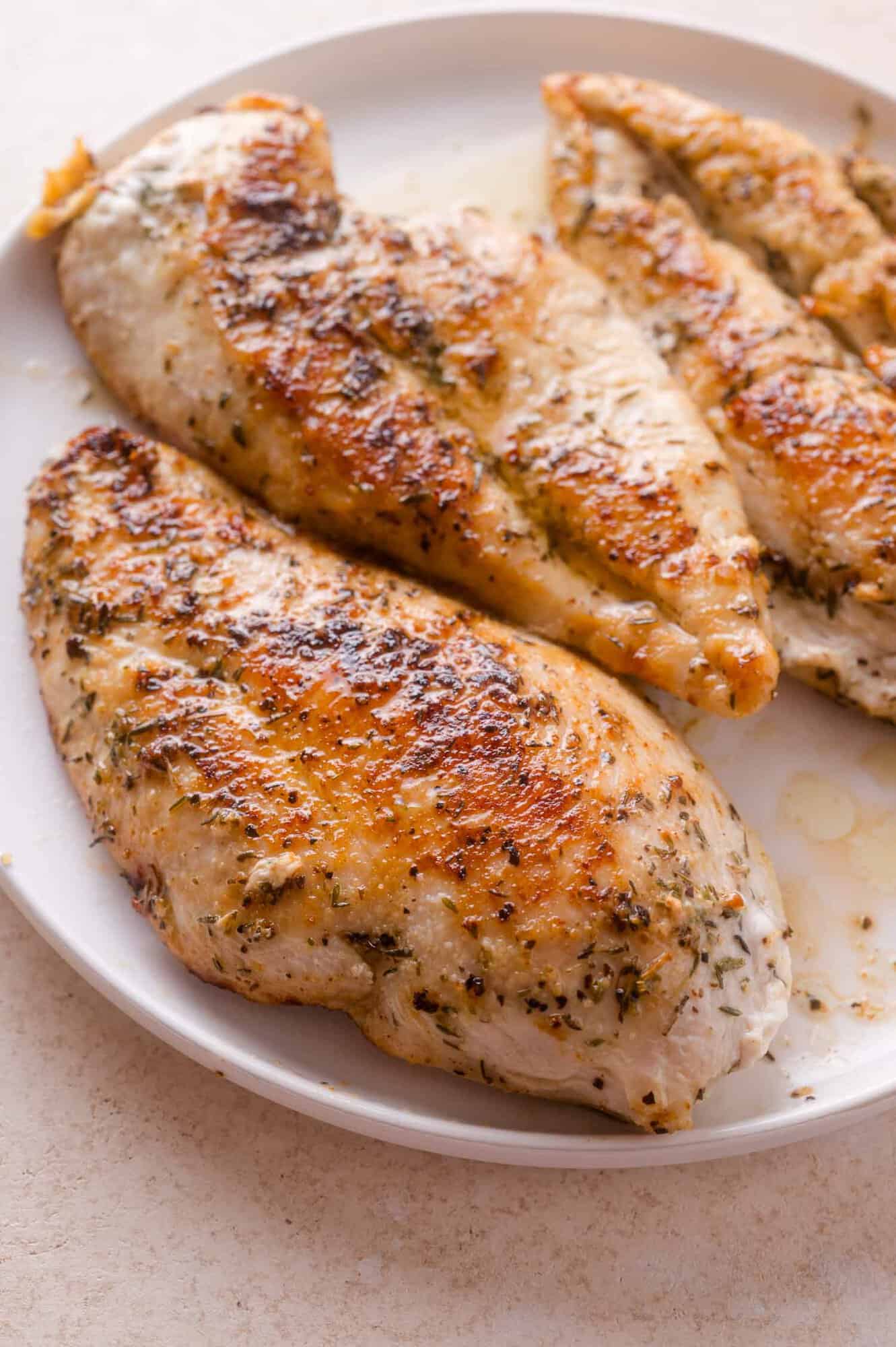 Three cooked, seasoned chicken breasts with a golden-brown crust are arranged on a white plate.