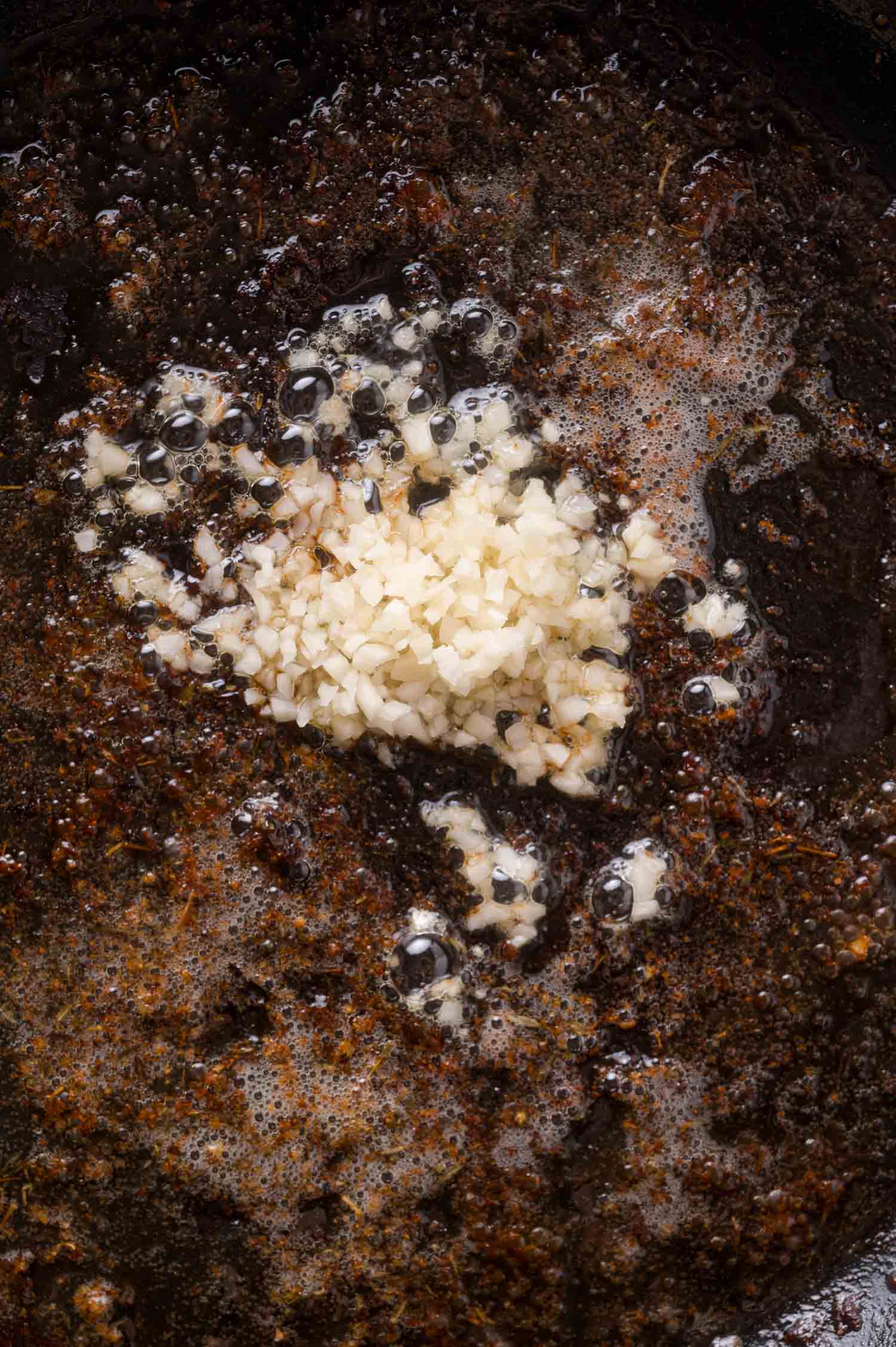Minced garlic sizzling in a skillet with melted butter and browned bits on the surface.