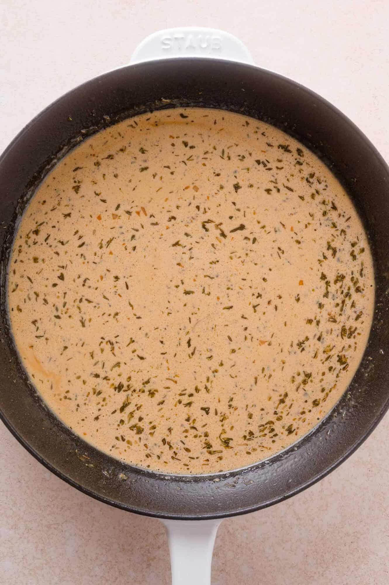 A black pan with a creamy, light brown sauce speckled with herbs, shown from above on a light countertop.