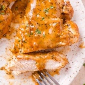 Close-up of sliced cooked chicken breast covered in a creamy apple cider cream sauce, garnished with chopped parsley, on a white plate with a fork.