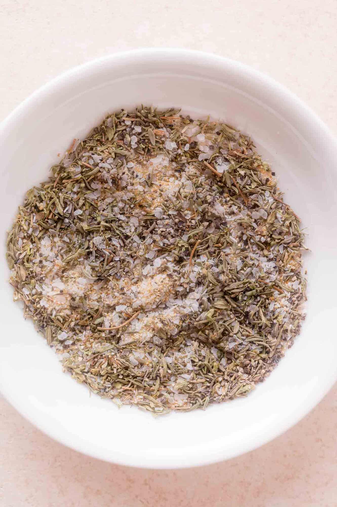 A white bowl filled with a dry herb and salt mixture, seen from above, on a light-colored surface.