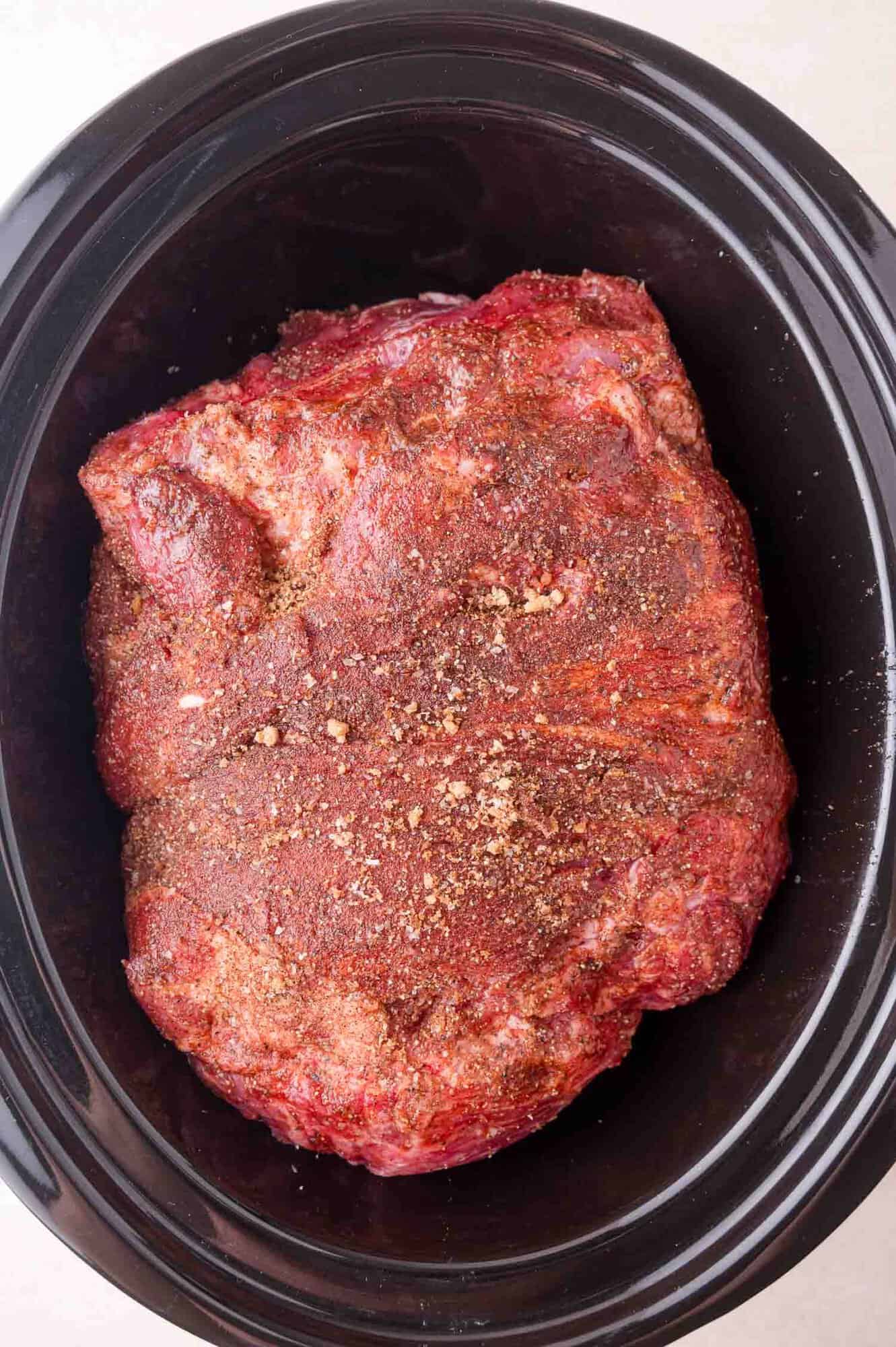 Raw seasoned meat placed inside a black slow cooker, ready to be cooked.