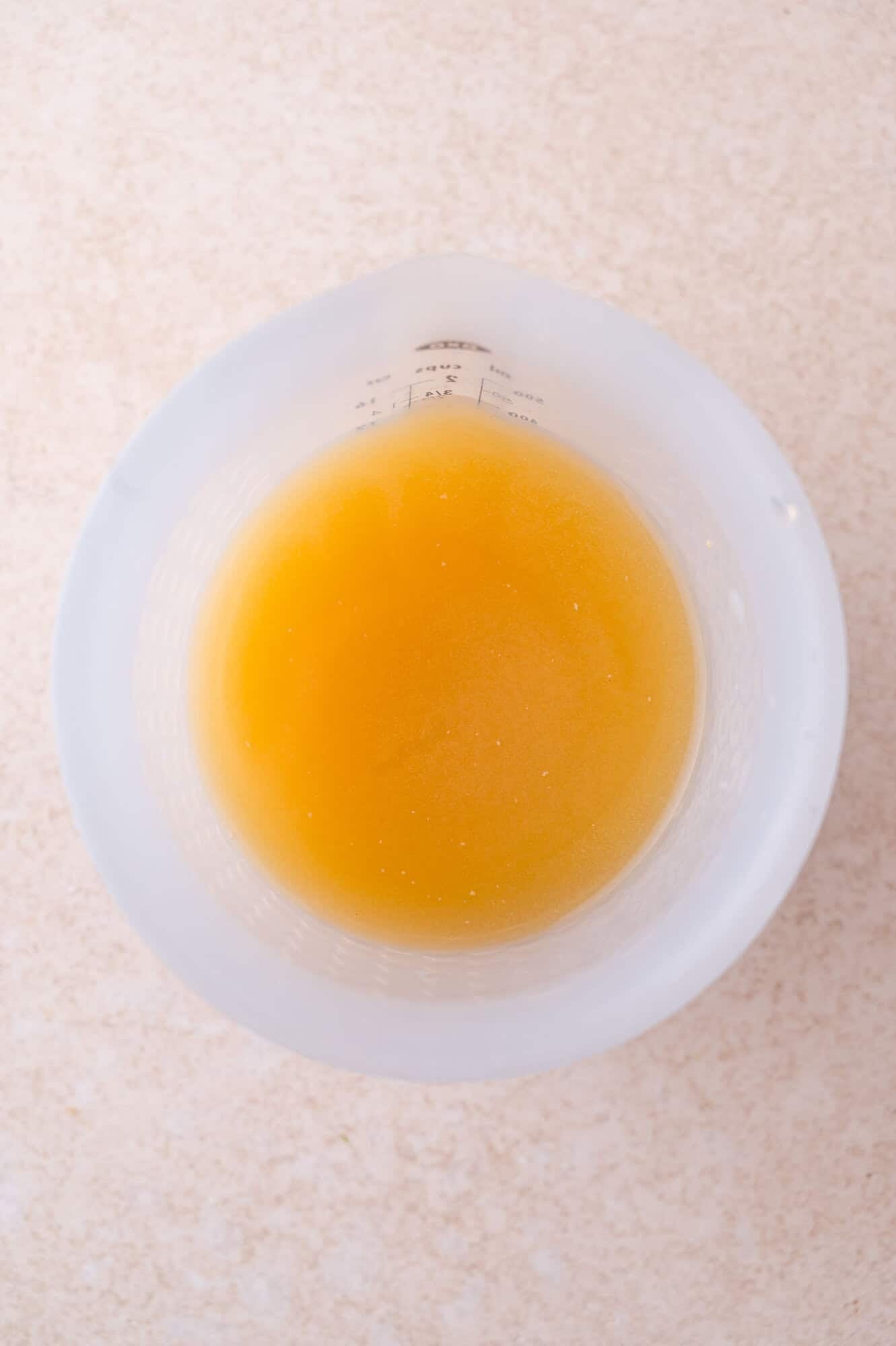 A clear measuring cup filled with a yellow-orange liquid, viewed from above on a light-colored surface.