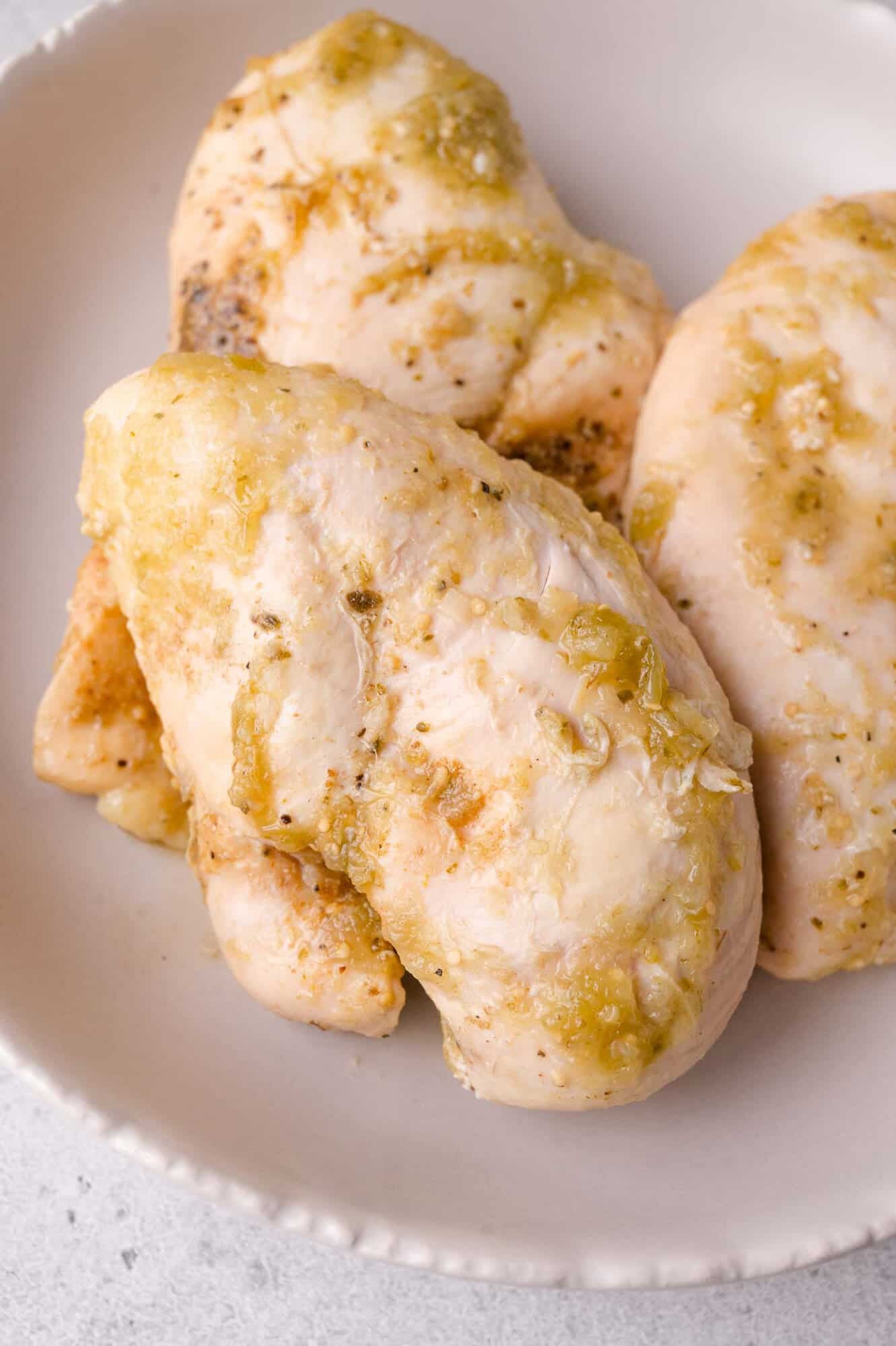Three cooked chicken breasts seasoned with herbs and spices on a white plate.