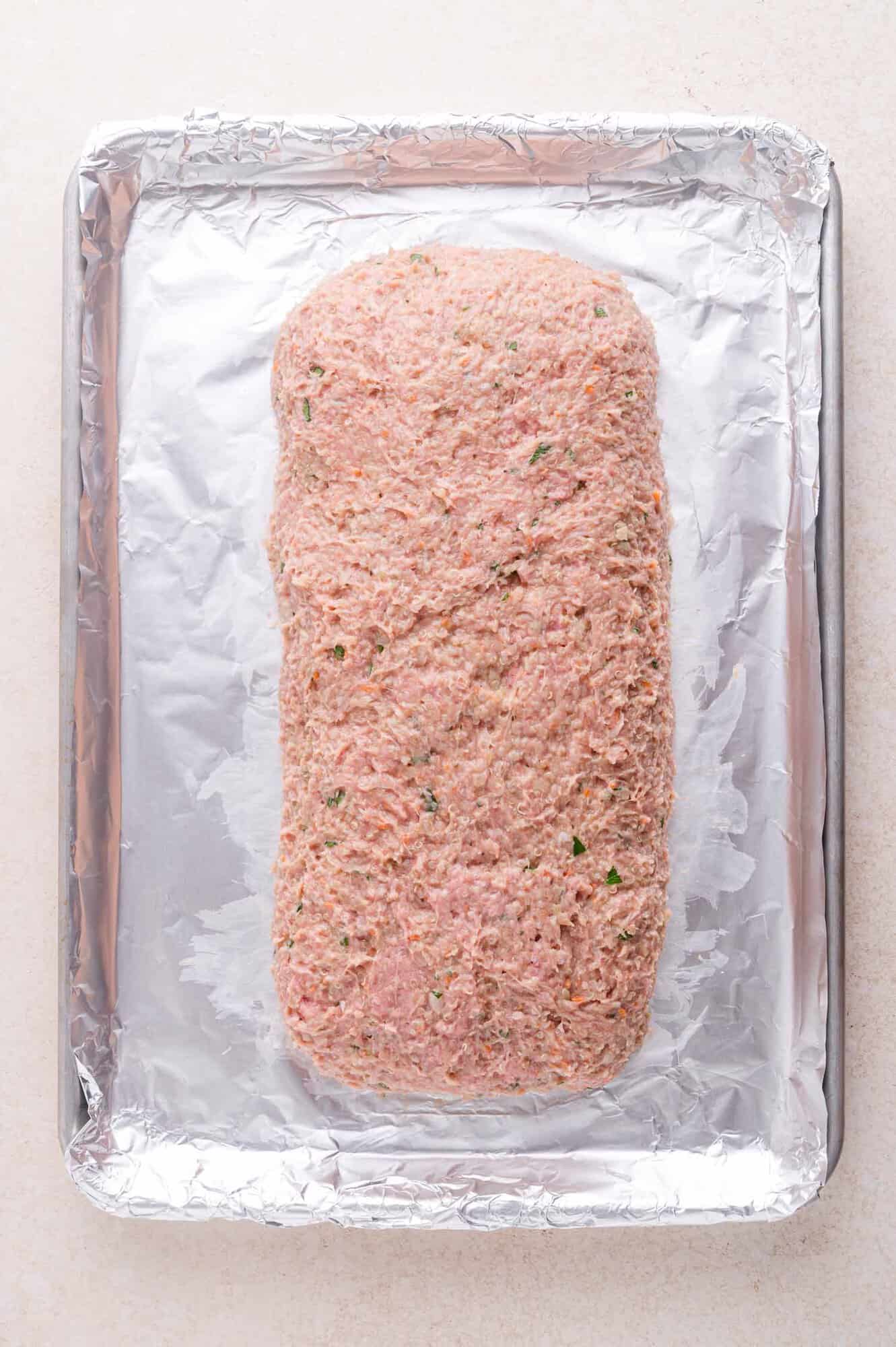 Uncooked meatloaf mixture shaped into a loaf on a foil-lined baking sheet.