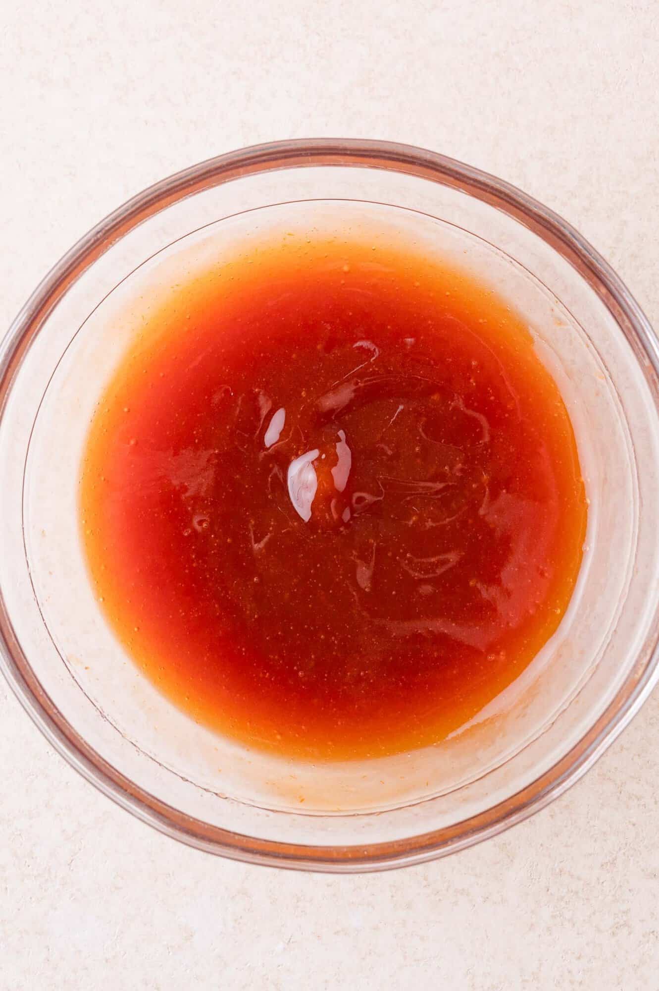A clear glass bowl filled with orange-red glaze on a light-colored surface.