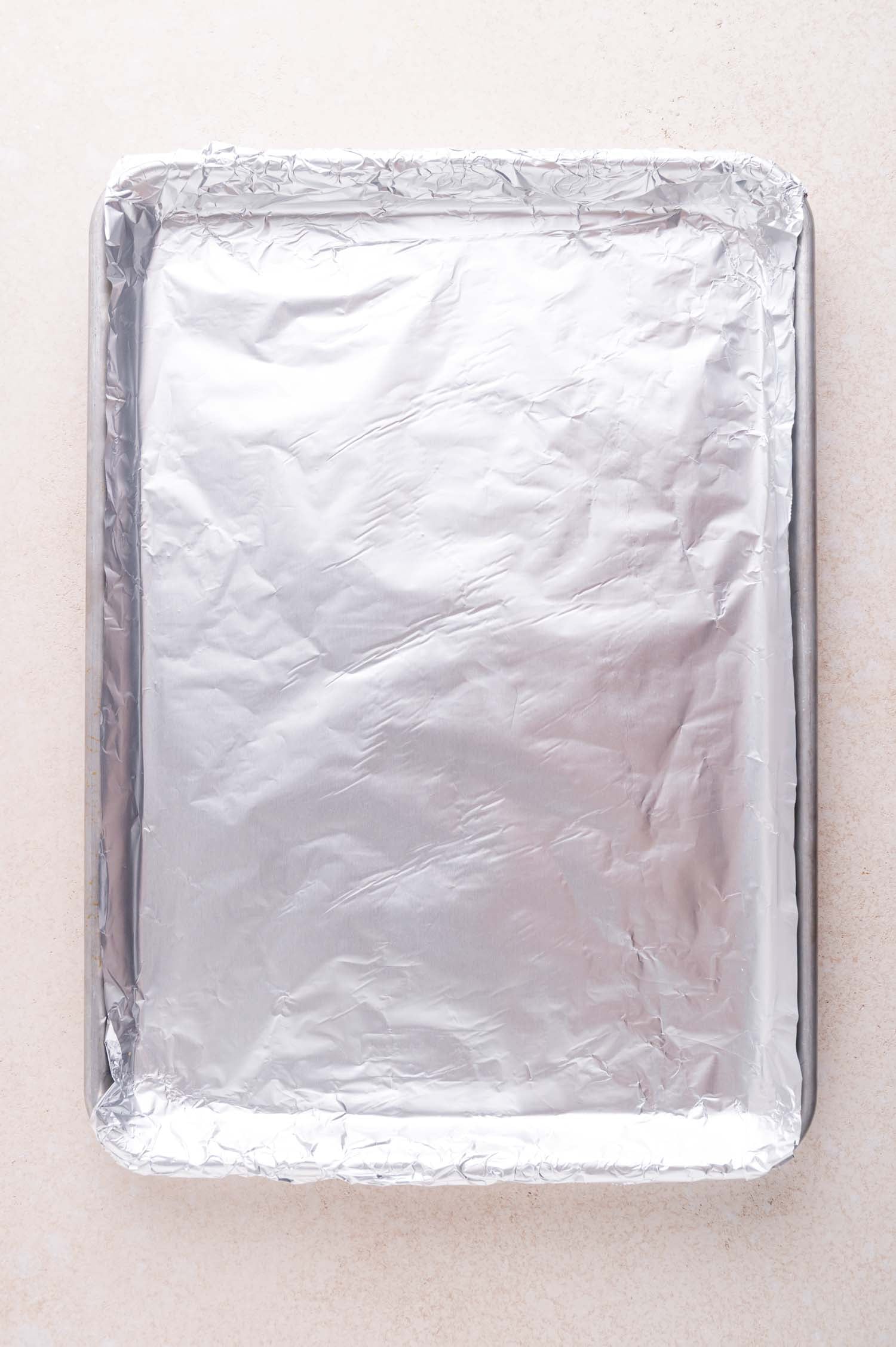 A rectangular baking sheet lined with aluminum foil sits on a light-colored surface.