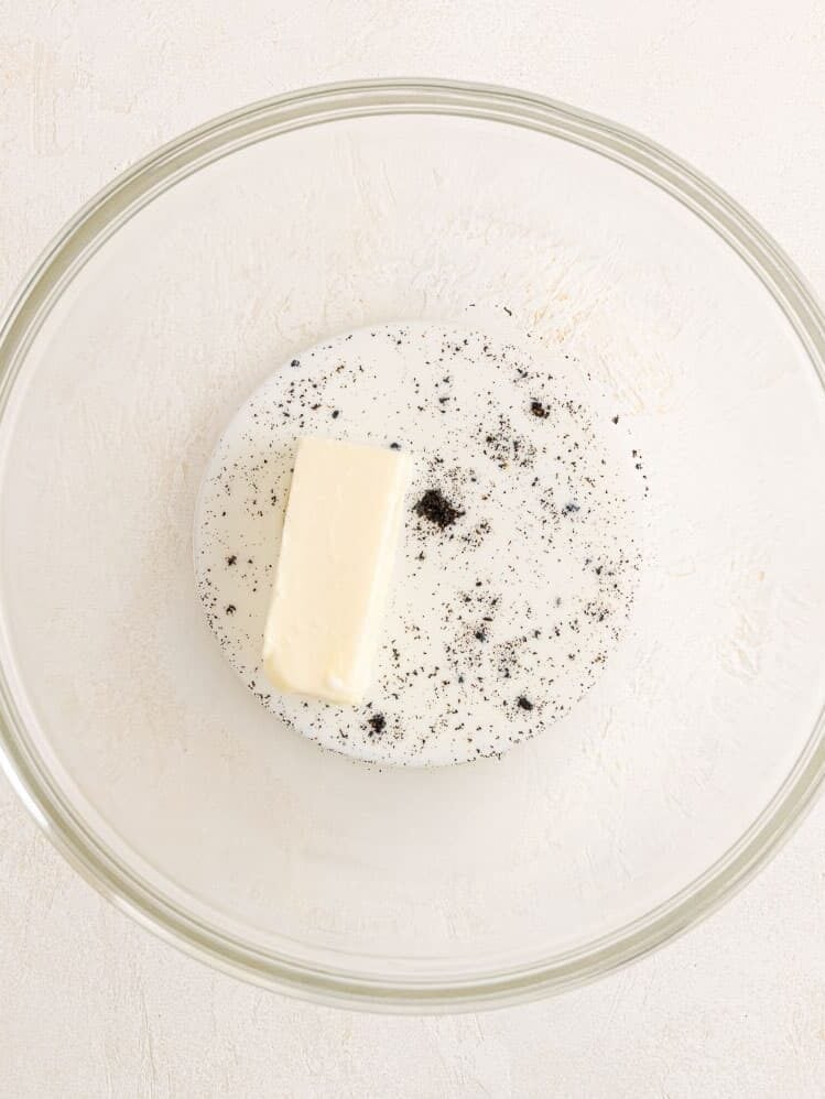 Butter, vanilla beans, and cream combined in a glass mixing bowl.