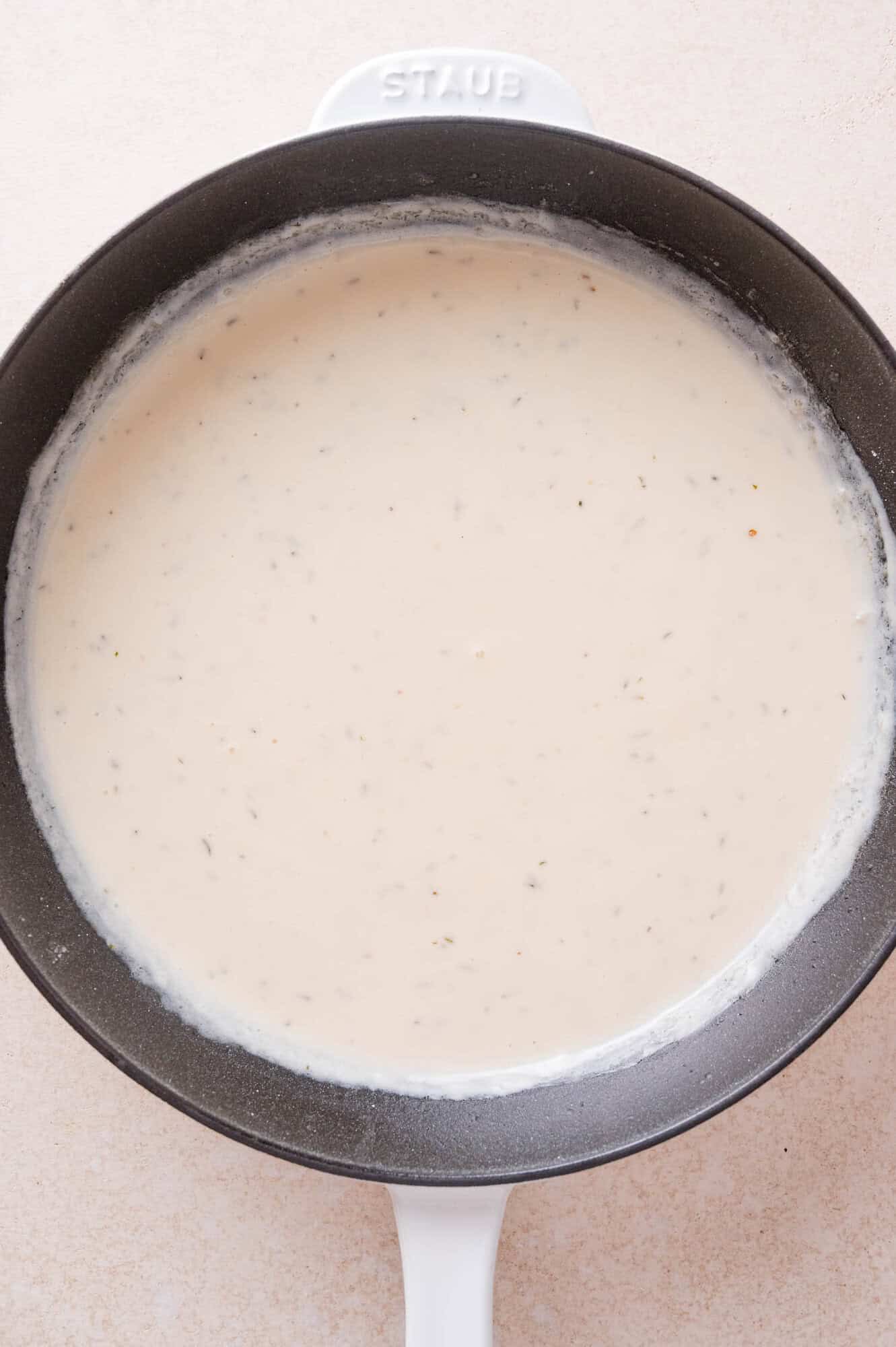 A cream-based sauce with herbs in a Staub skillet, viewed from above.