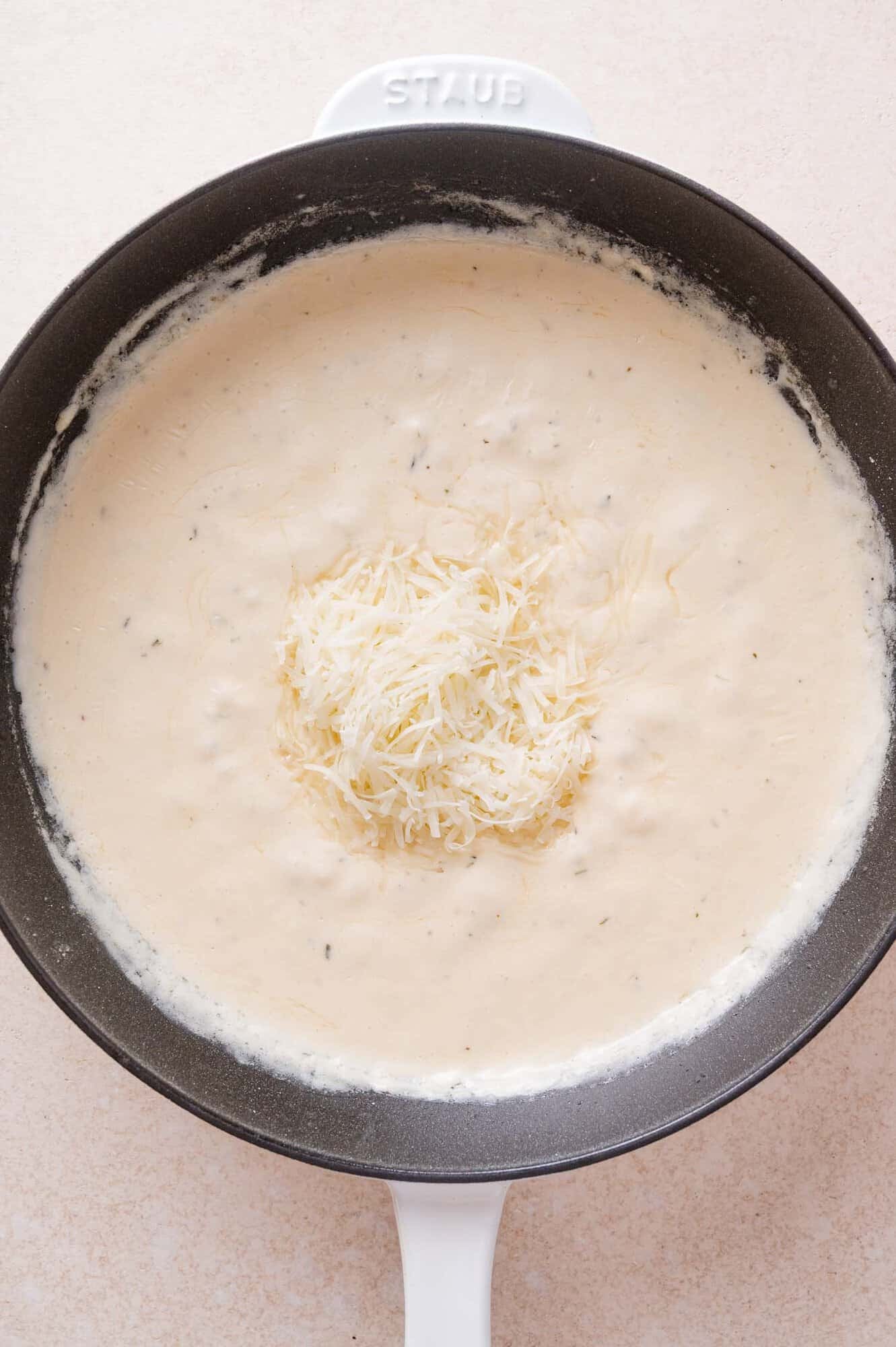 A pile of shredded cheese in the center of a creamy sauce in a skillet.