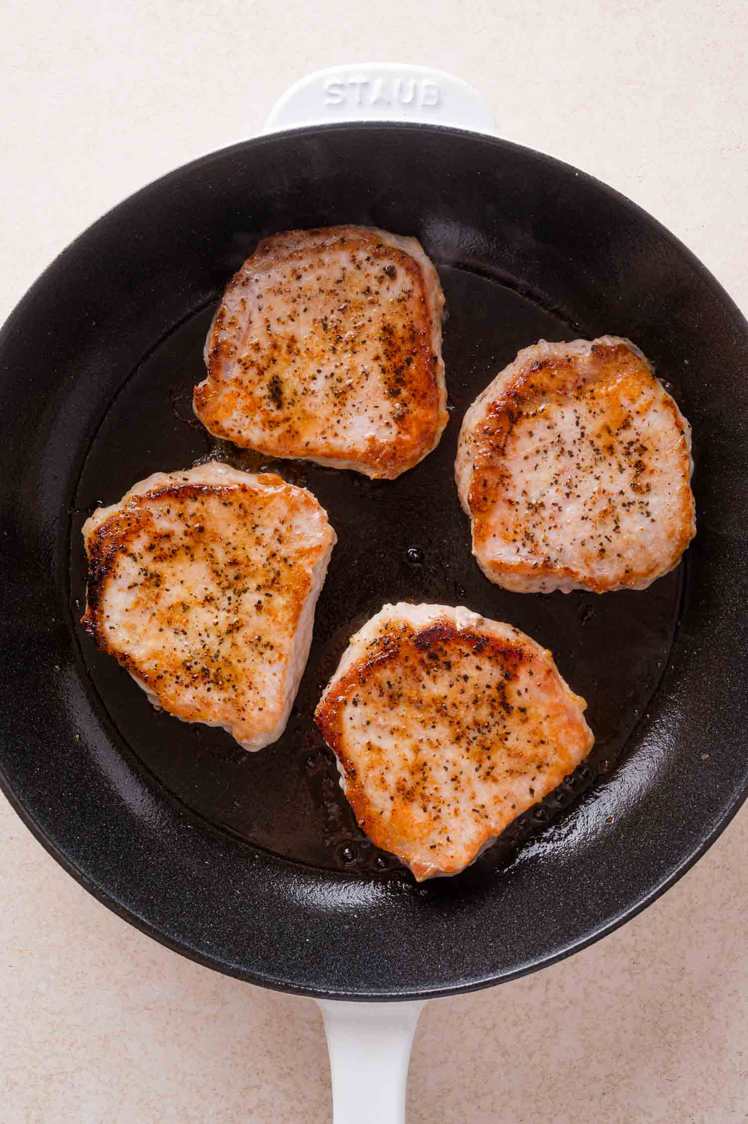Four seasoned pork chops searing in a black skillet.