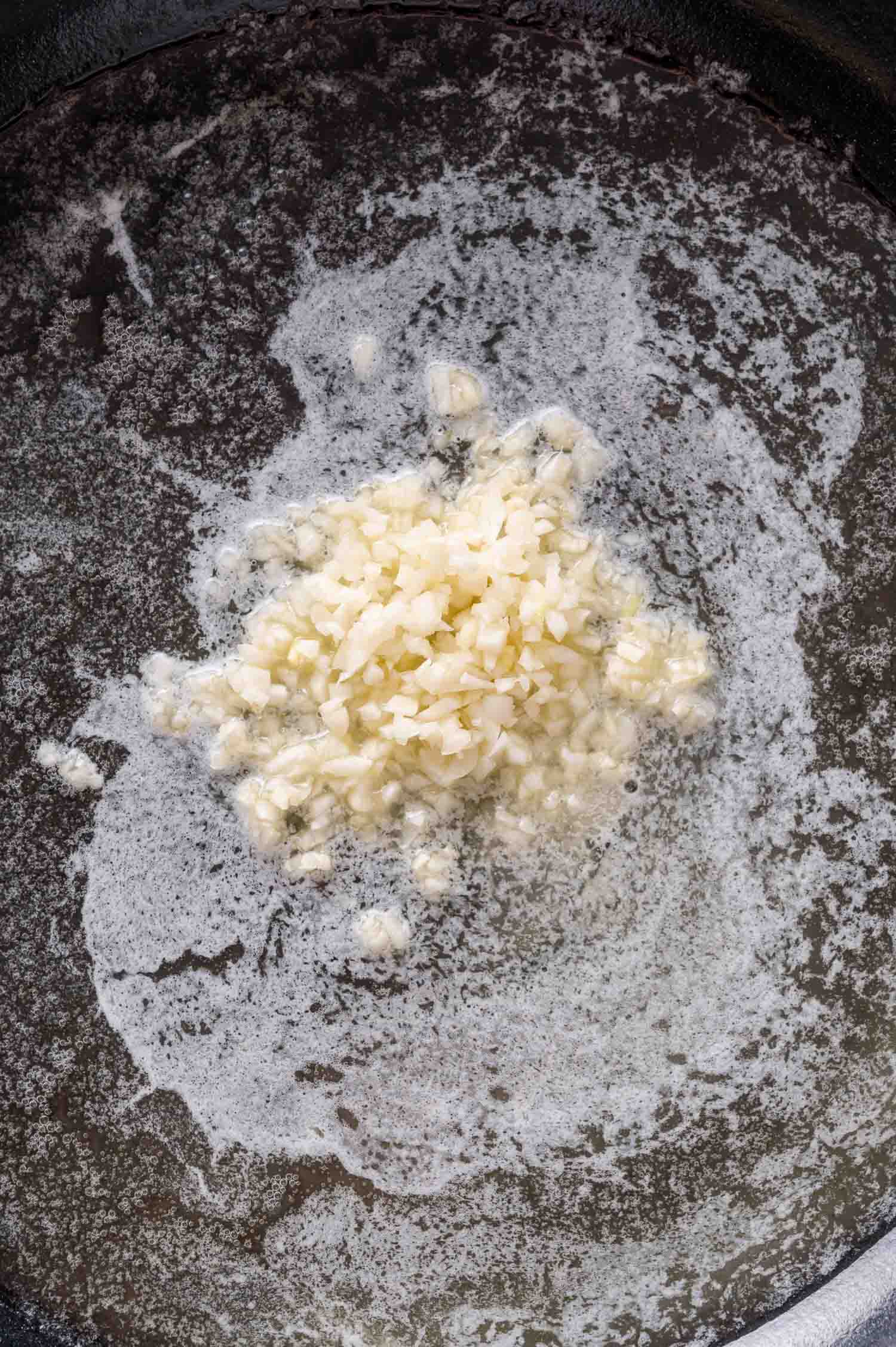 Minced garlic sautéing in melted butter in a dark skillet.