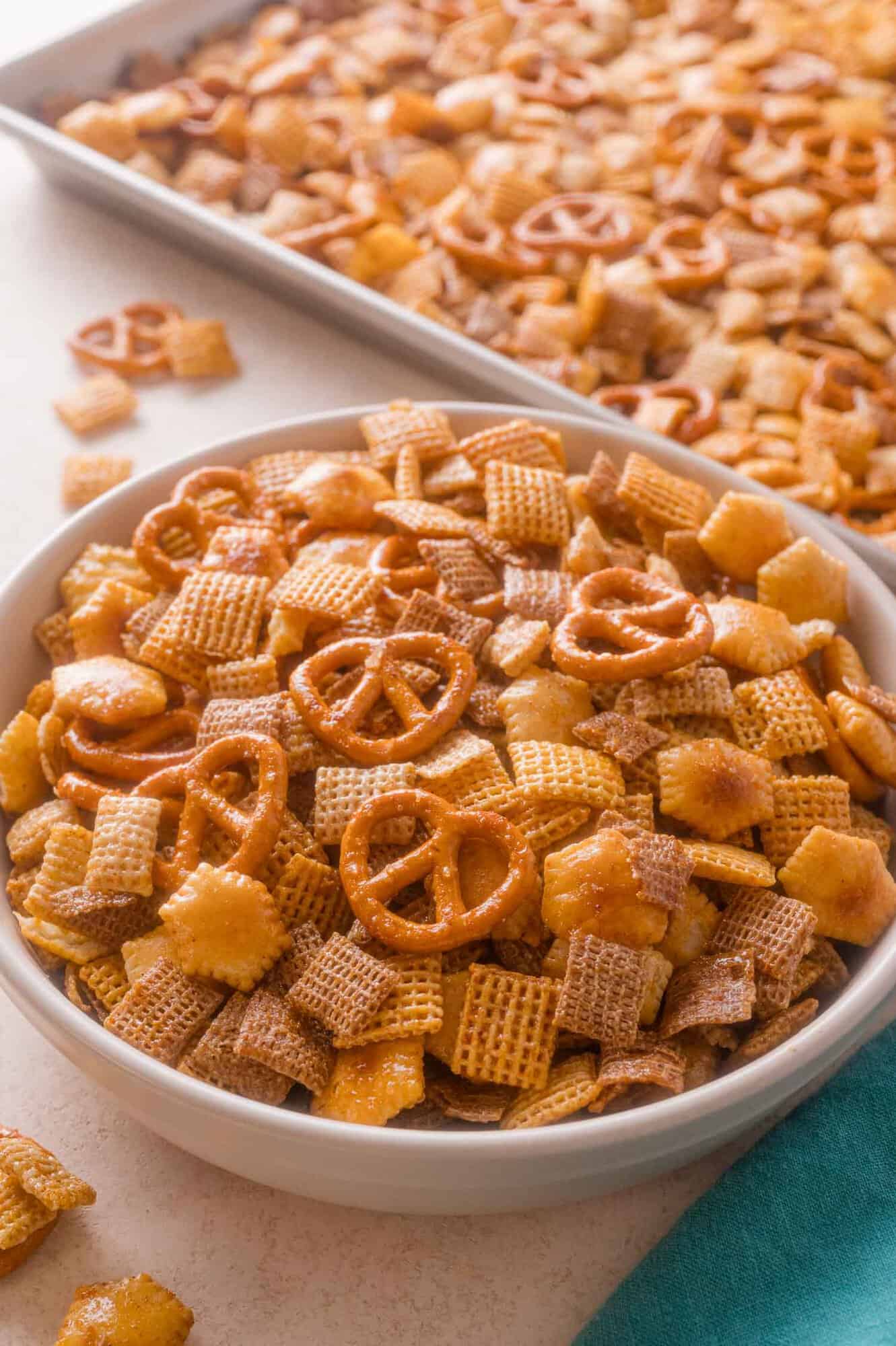 A white bowl filled with hot honey Chex party mix containing pretzels, square cereal pieces, and crackers.