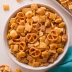 A bowl filled with a snack mix containing square cereal, pretzels, and crackers.