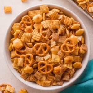 A bowl filled with a snack mix containing square cereal, pretzels, and crackers.