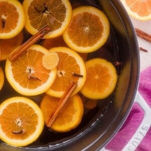 Orange slices, cinnamon sticks, and cloves floating in a pot of apple cider.