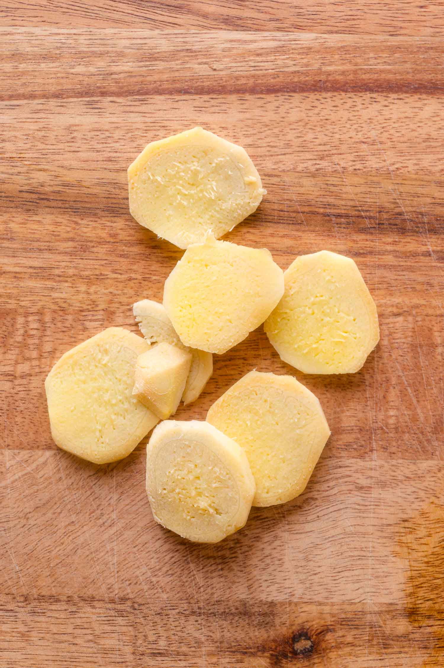 Several slices of peeled ginger root on a wooden cutting board.